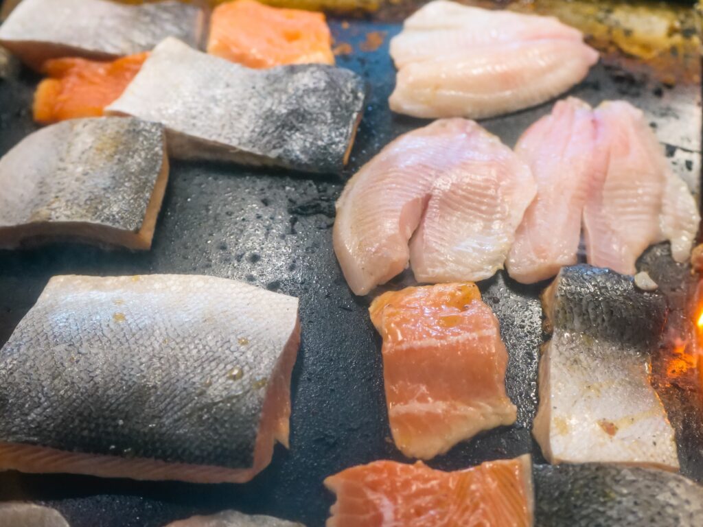 A picture of Salmon and Cod fish pieces on a grill