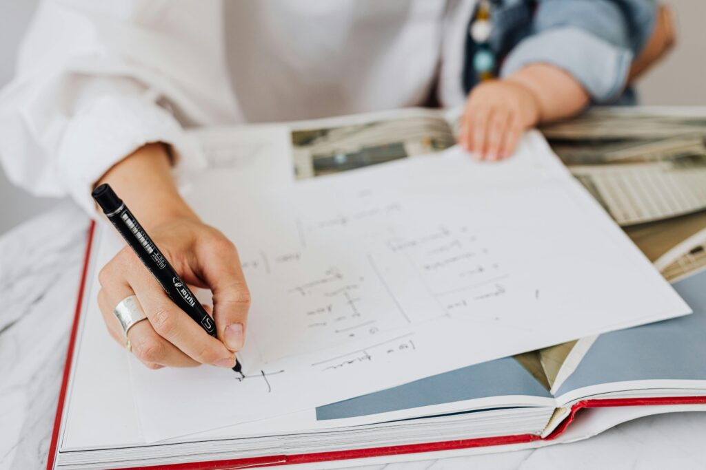 How To Calculate Your Macros For The Keto Diet. A woman calculating her Macros for her Keto Diet on a piece of paper which is on top of a book.