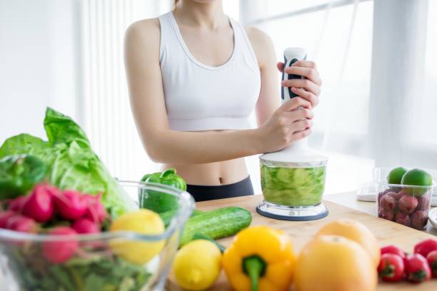 Woman making healthy green smoothie with blender in kitchen